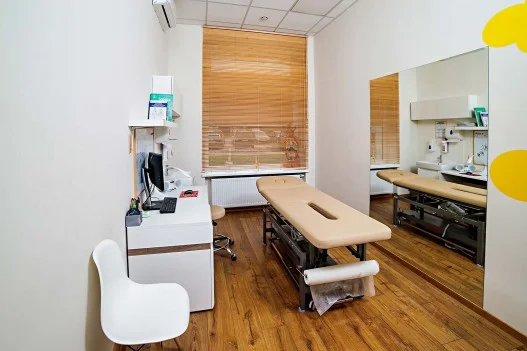 Gabinet fizjoterapeuty w Łodzi, wyposażenie to łóżko rehabilitacyjne, biurko, duże lustro oraz siedzenia, klimatyzacja